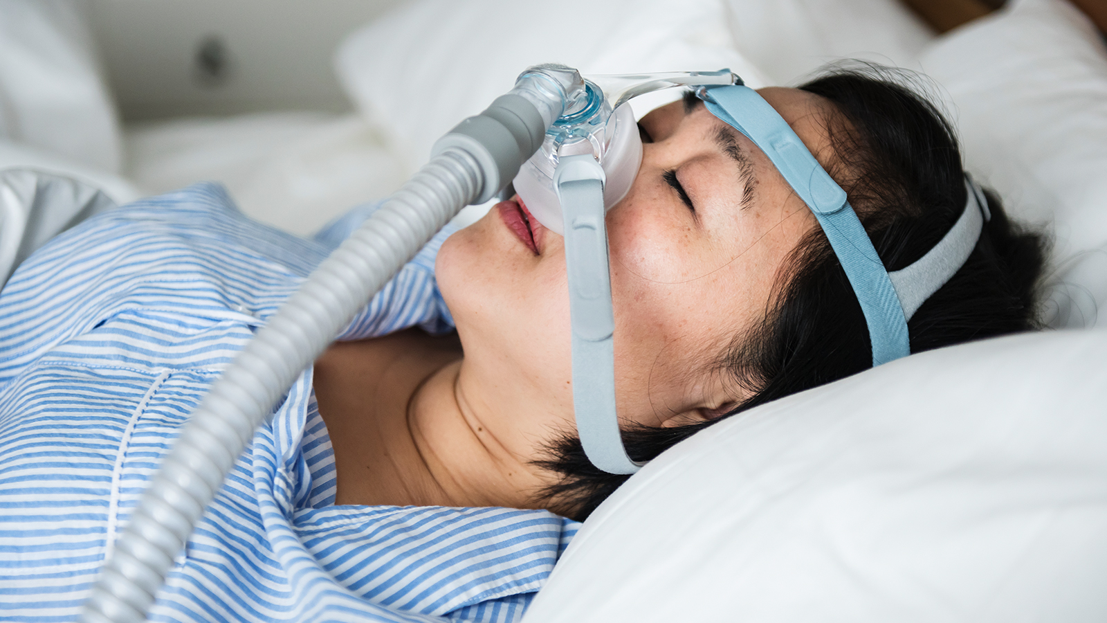 A woman asleep in bed wearing a CPAP nasal mask and hose