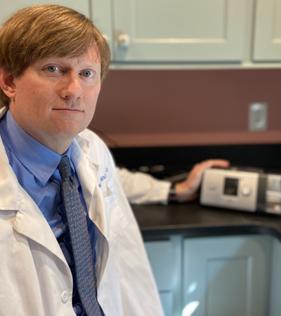 Dr. Dewey McWhirter beside a CPAP machine on the exam room counter