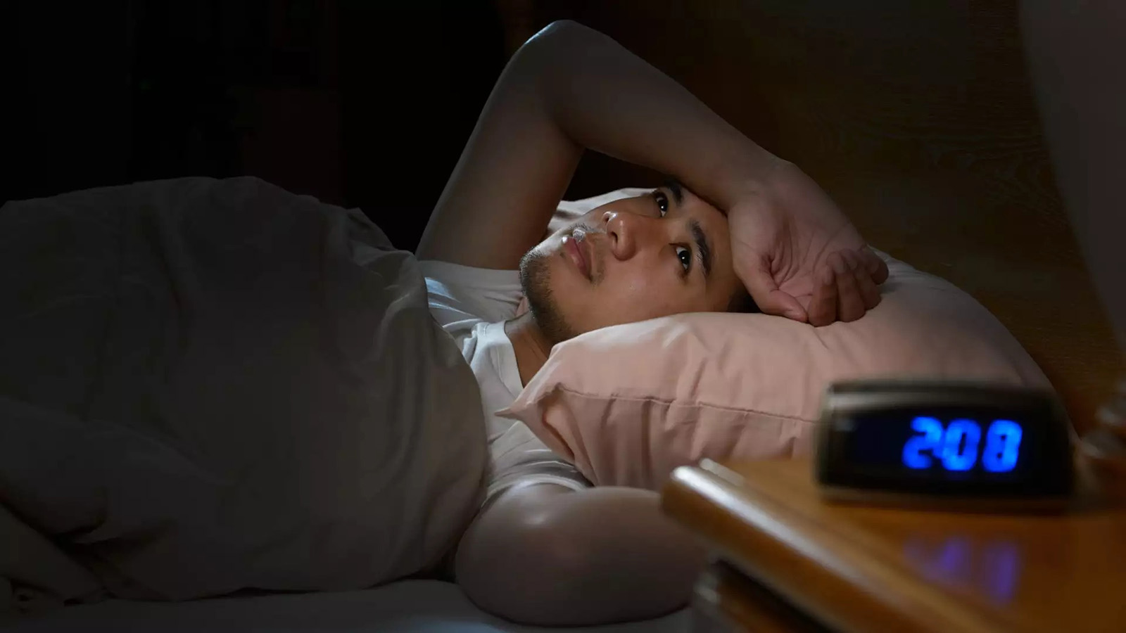 A man lying awake in bed at night, the clock beside him reading 2:00